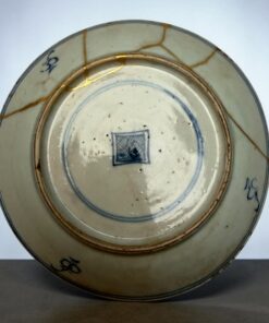 Close-up of a ceramic plate repaired with gold seams (kintsugi), showing blue rim and cracks in the glaze.