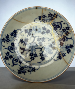 Decorative blue-and-white porcelain plate with gold crack repair (kintsugi), shown from the edge against a gray background