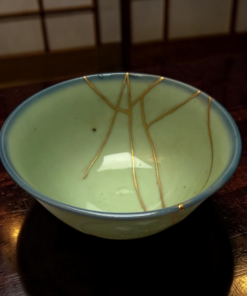 Close-up of a light green ceramic bowl with gold decorative lines resting on a dark wooden table edge visible in the frame.