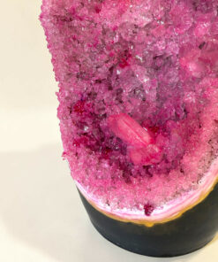 Close-up of a bright pink crystal cluster topping on a dark plate, filling most of the frame against a light background.