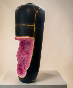 Black vase-like sculpture with a pink crystal inlay along its edge, displayed on a light pedestal.