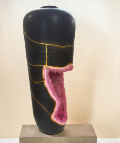 Abstract black sculpture with gold veining and a pink geode insertion, on a concrete pedestal.