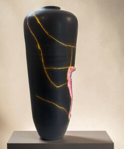 Black ceramic vase with gold veining placed on a gray pedestal against a neutral wall.