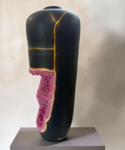 Tall black ceramic vase with pink glaze dripping down the side, accented by thin gold lines, displayed on a gray pedestal.