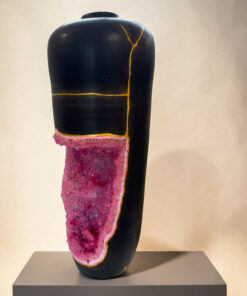 Black ceramic vase with gold crack lines and a pink crystalline base on a gray pedestal.