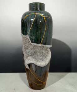 Dark green bottle wrapped in salt crystals with a yellow string, set against a neutral gray background.