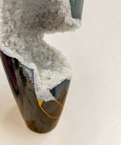 Close-up of a dark, glossy ceramic vase with a rough white crystal crust along its edge.