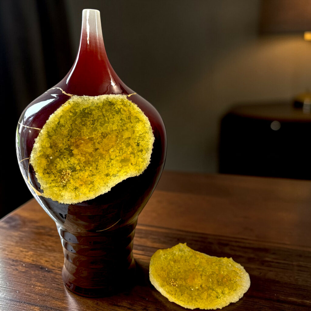 Close-up of a dark glass bottle resting on a wooden table with two yellow sugar-crystal cookies stuck to its side, blurred background.