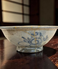 Close-up of a ceramic bowl with blue floral glaze and gold-toned cracks, resting on a dark wooden table.