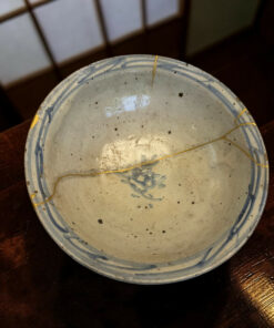Close-up of a speckled ceramic plate with a blue rim placed on a dark wooden table, with a thin gold string resting on it.