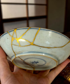 Hands cradle a pale blue ceramic plate with gold crackle lines and blue trim, resting on a wooden surface