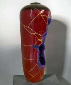 Close-up of a red ceramic vase with a large purple glaze crack running down its side, displayed on a dark pedestal.