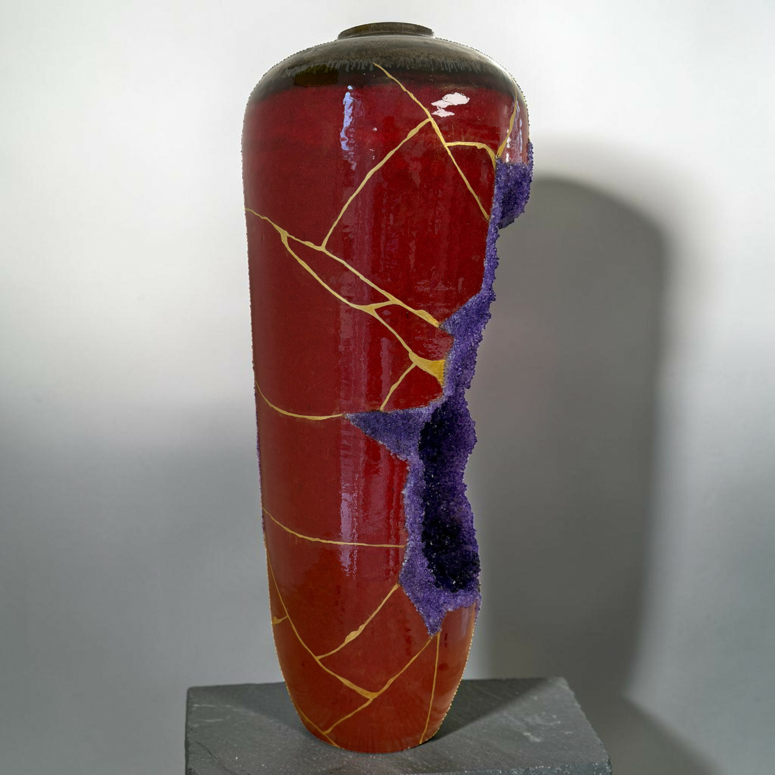 IMG_3235-Photoroom | Kintsugi by Myriam GREFF Close-up of a red ceramic vase with a large purple glaze crack running down its side, displayed on a dark pedestal.