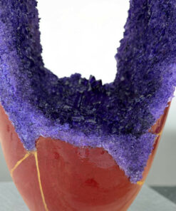 Close-up of a ring-shaped pastry coated in chunky purple sugar crystals, showing a rough, sparkling texture.