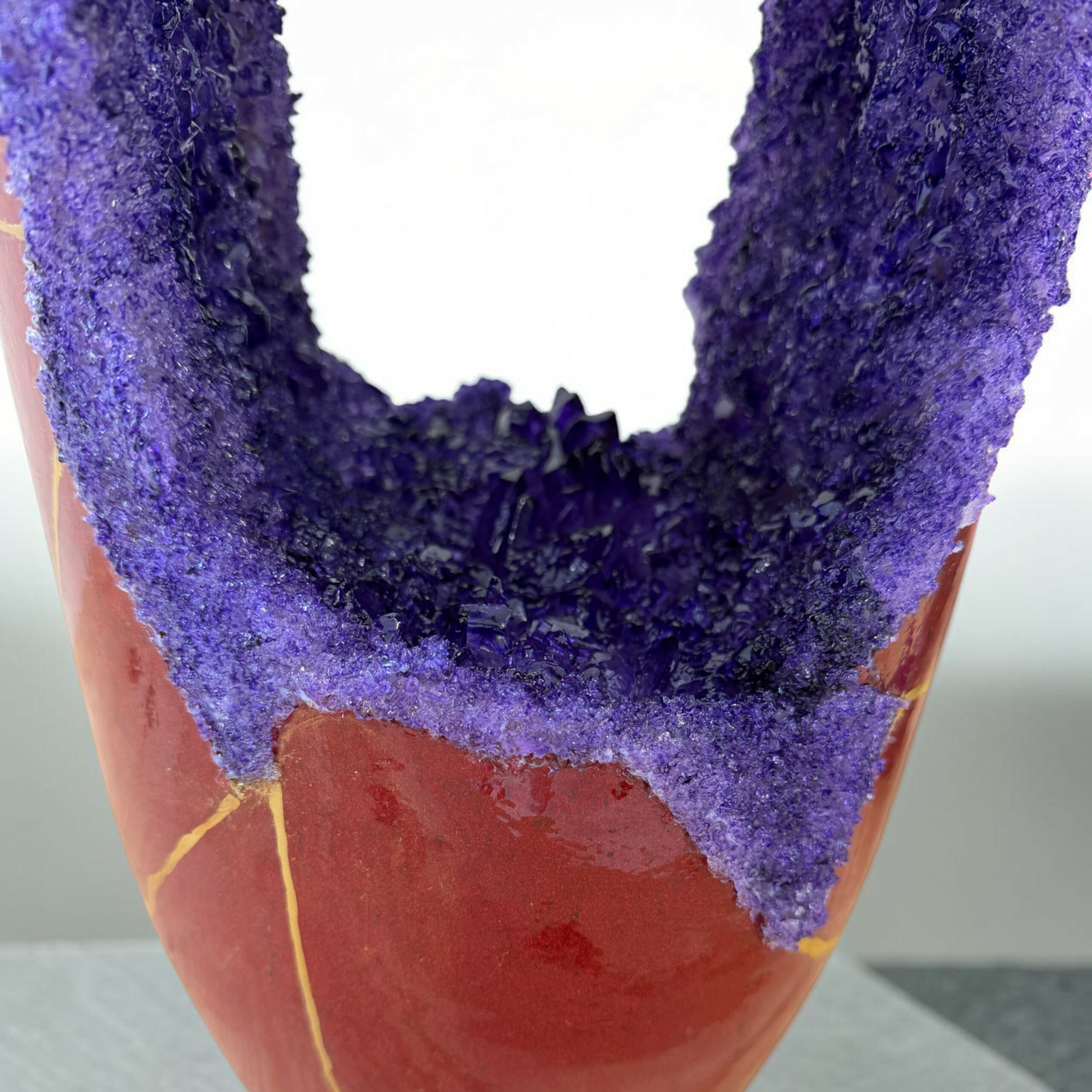 IMG_3236-Photoroom | Kintsugi by Myriam GREFF Close-up of a ring-shaped pastry coated in chunky purple sugar crystals, showing a rough, sparkling texture.