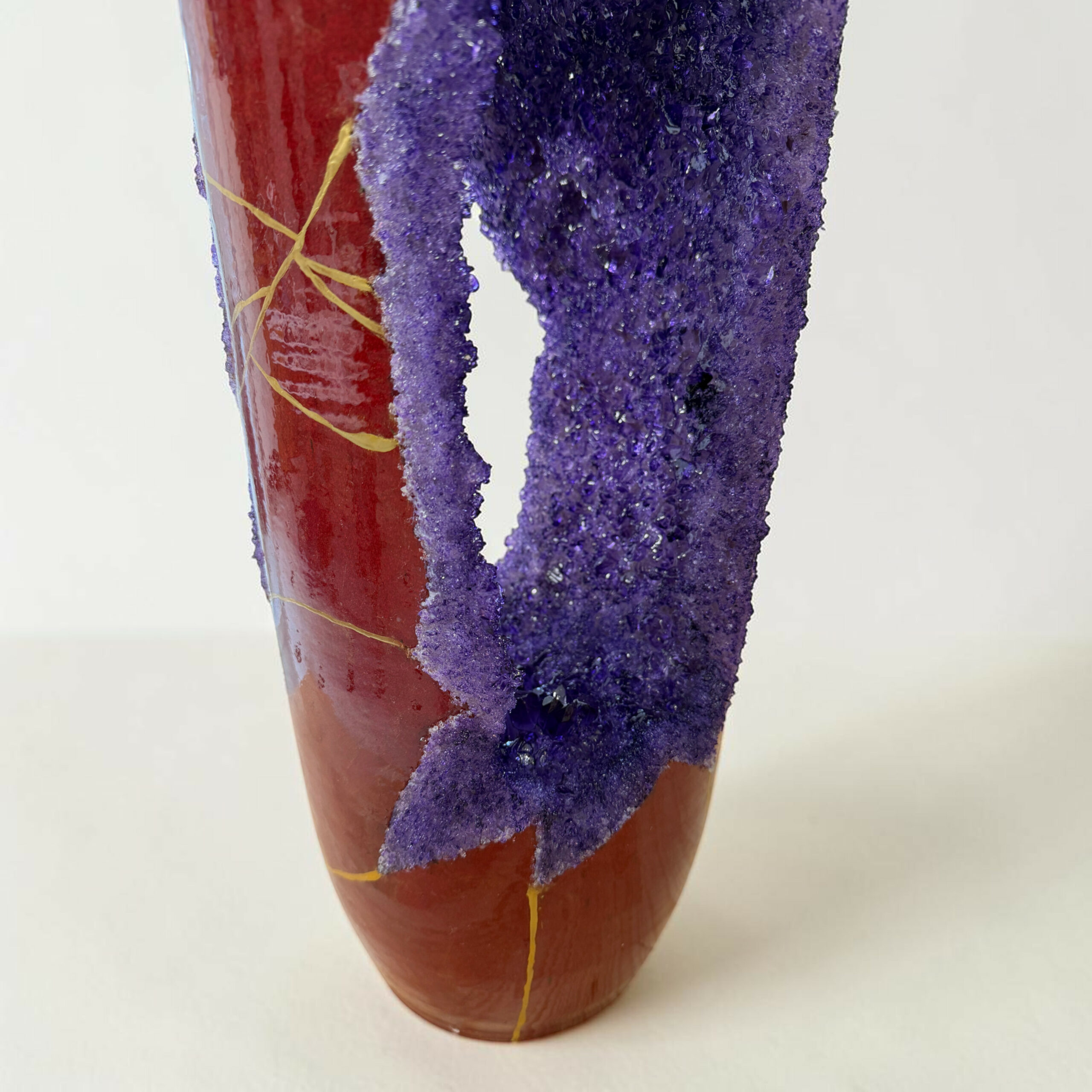 IMG_3239-Photoroom | Kintsugi by Myriam GREFF Close-up of a red ceramic vase wrapped with purple glittery material and yellow string against a pale background.