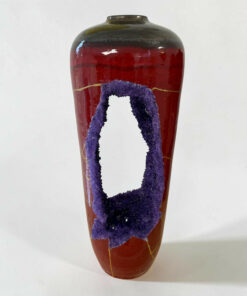 Close-up of a tall ceramic vase with a glossy red body and purple crackled ribbon design running down its sides, against a pale background.