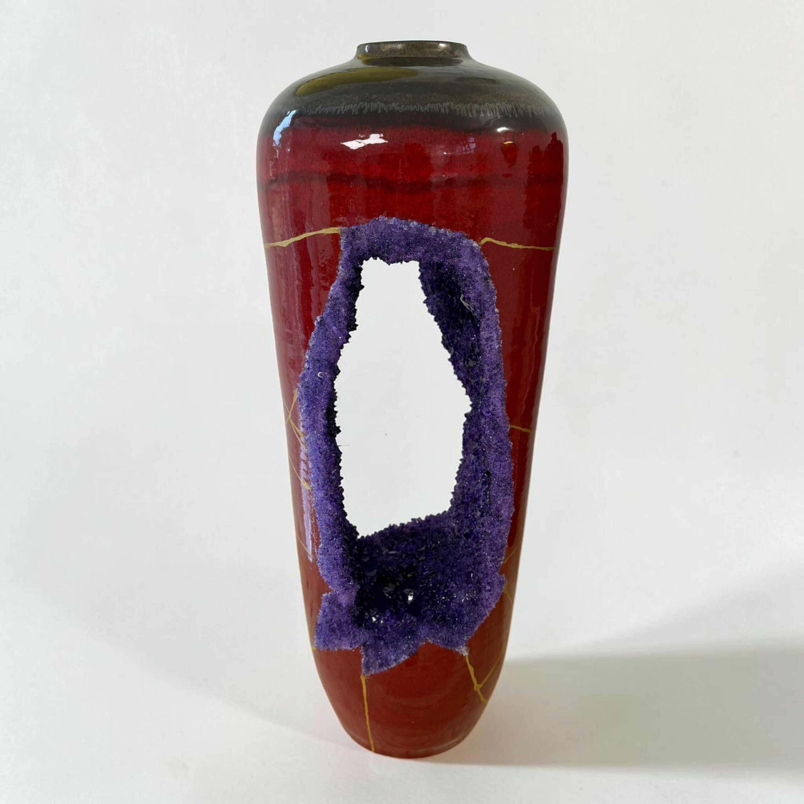 IMG_3240-Photoroom | Kintsugi by Myriam GREFF Close-up of a tall ceramic vase with a glossy red body and purple crackled ribbon design running down its sides, against a pale background.
