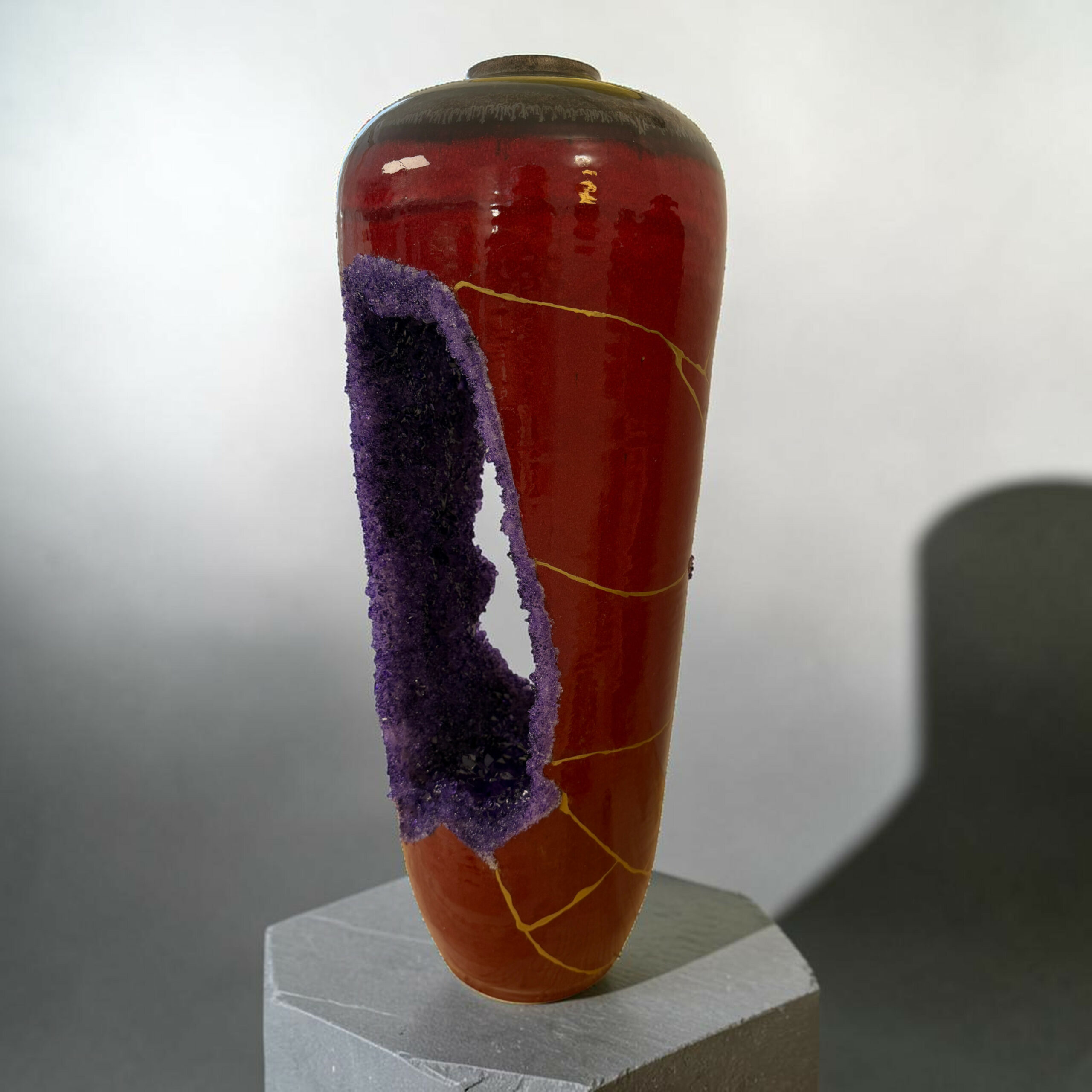 IMG_3242-Photoroom | Kintsugi by Myriam GREFF Red ceramic vase with purple crystallized deposits and a yellow line, displayed on a gray stepped pedestal.