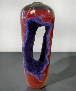 Decorative ceramic vase with purple textured loops wrapped around its middle against a gray background, hanging down like ropes.