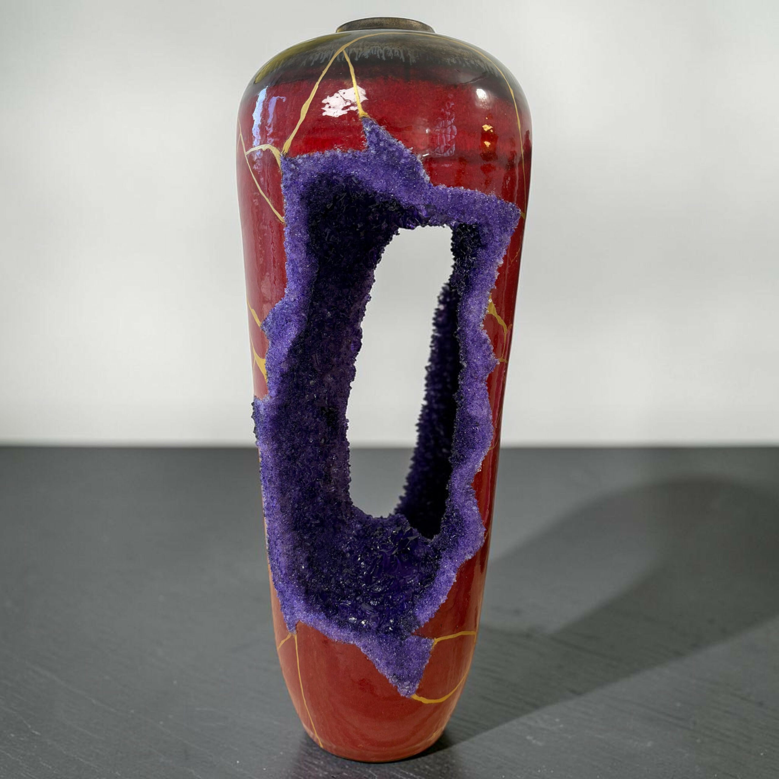 Mobilis In Immobile-Vase Geode- myriam GREFF | Kintsugi by Myriam GREFF Decorative ceramic vase with purple textured loops wrapped around its middle against a gray background, hanging down like ropes.