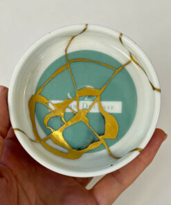Close-up of a ceramic plate with teal center and gold crackle pattern, held in a person's hands